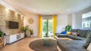 A modern living room with a stone wall, a flat-screen TV, a grey sofa, and a coffee table. - Villa Zupan by Villa Plus (Barici)