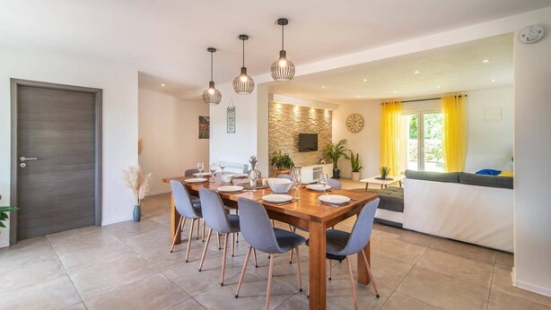 A dining area with a wooden table set for four, surrounded by six chairs. There are hanging pendant lights above the table. - Villa Zupan by Villa Plus (Barici)