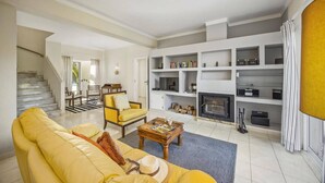 Uma sala de estar ampla com um sofá amarelo, uma lareira e uma escada que leva a outro nível.