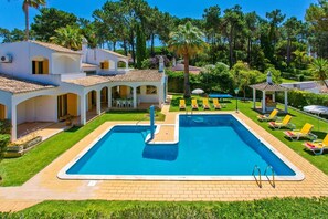 A pool area with a rectangular pool, lounge chairs, and a covered seating area.