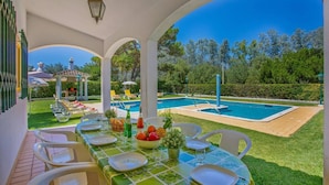 Un espacio de comedor al aire libre techado, con una piscina al fondo.