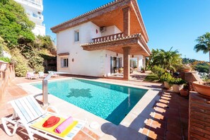 Eine zweistöckige Villa mit Swimmingpool, Sitzgelegenheiten im Freien und einem Garten.