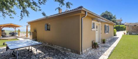 A single-story building with a stone-paved patio, a small garden, and a pergola.