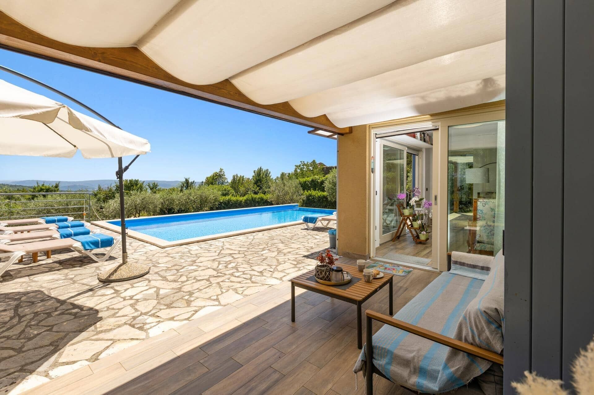 A poolside area with lounge chairs, a table with a teapot, and a view of the landscape.