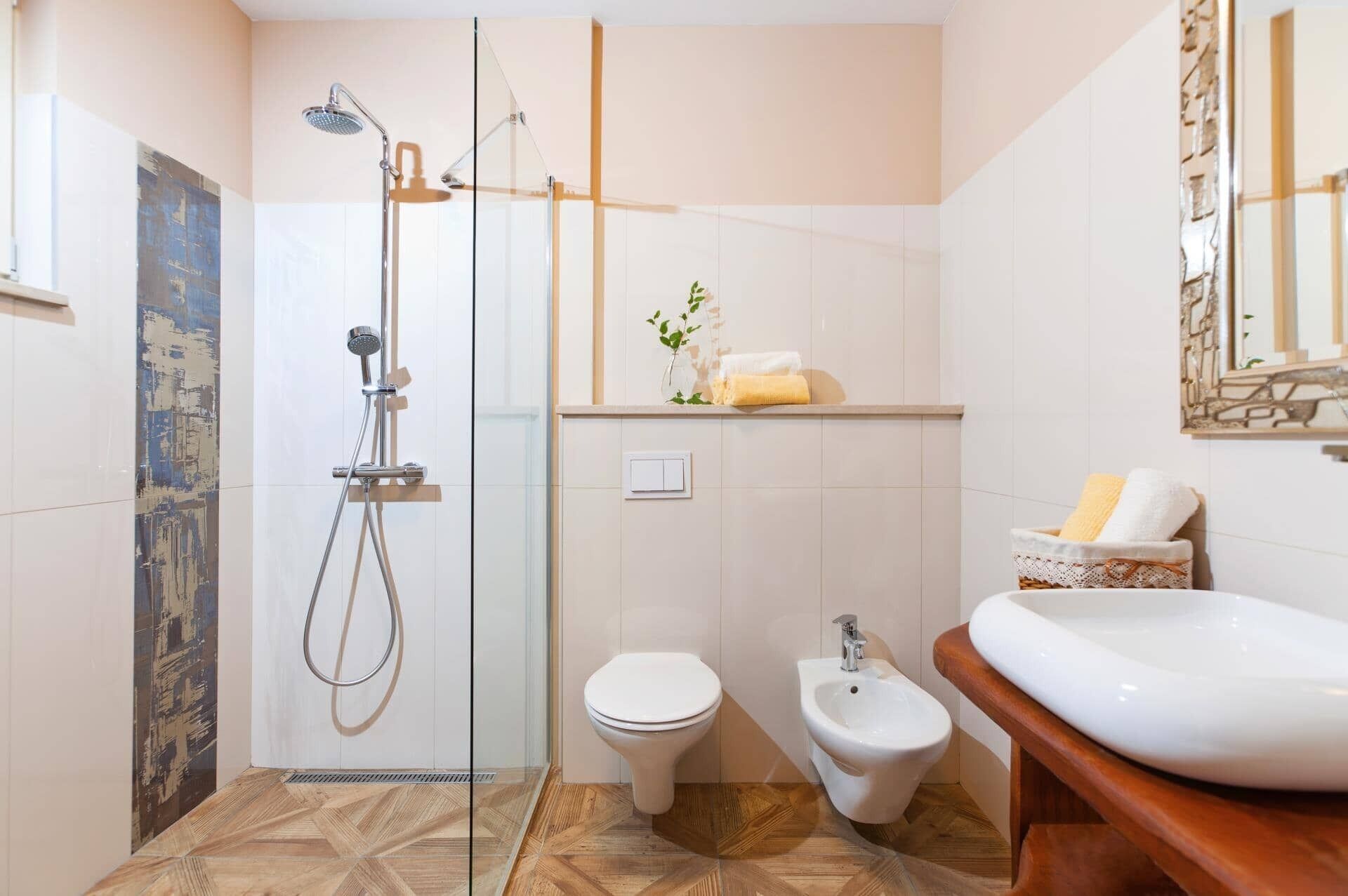 A bathroom with a glass shower enclosure, a toilet, a bidet, and a sink with a wooden countertop.