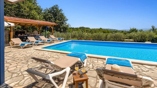 Zona de piscina con sillones de descanso, una barbacoa y vistas al paisaje.
