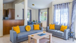 A living room with two grey sofas, yellow cushions, a wooden coffee table, and a dining area with a table and chairs.