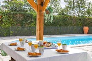Disposição para café da manhã à beira da piscina, com croissants, suco de laranja e xícaras de café.