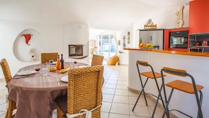A dining area with a round table, wicker chairs, and a kitchen with a red accent wall. - Villa Les Arches by Villa Plus (Villedaigne)