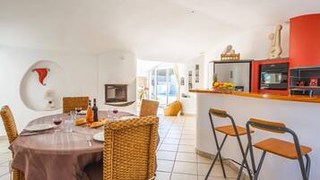 Un coin repas avec une table ronde, des chaises en osier et une cuisine dont un mur est peint en rouge.