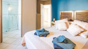 A hotel room with a bed, towels, a nightstand, a lamp, and a glass-enclosed shower area. - Villa Les Arches by Villa Plus (Villedaigne)