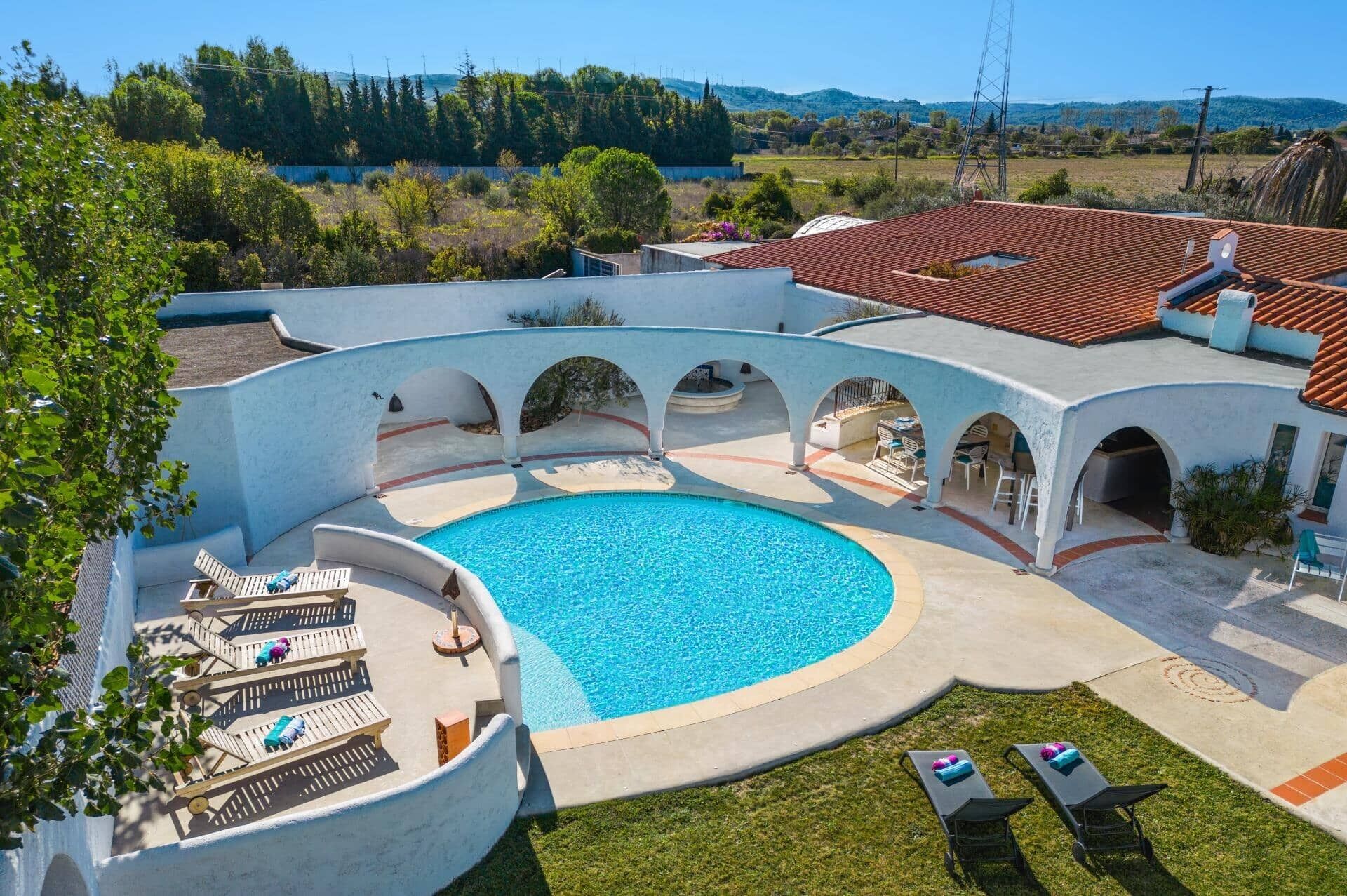 Une piscine au design incurvé, entourée de chaises longues et d’un espace patio couvert.