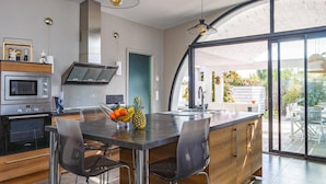A modern kitchen with a central island, stainless steel appliances, and a large window overlooking a garden. - Villa Saffron by Villa Plus (Villedaigne)