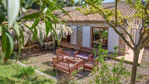 A stone building with a tiled roof, a patio with wooden furniture, and a garden with trees and shrubs. - Villa Fraisse by Villa Plus (Fraissé-des-Corbières)