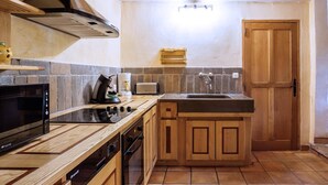 A compact kitchen with a microwave, stove, sink, and wooden cabinets. - Villa Fraisse by Villa Plus (Fraissé-des-Corbières)