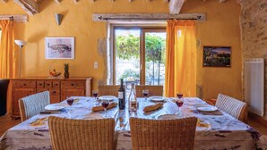 A dining room with a table set for four, wicker chairs, a wooden cabinet, and a painting on the wall. - Villa Fraisse by Villa Plus (Fraissé-des-Corbières)