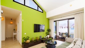 Ein modernes Wohnzimmer mit grüner Akzentwand, einem Flachbildfernseher, einer Couch, einem Couchtisch und einem Essbereich mit Tisch und Stühlen.
