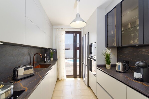 A modern kitchen with a marble countertop, stainless steel appliances, and a view to an outdoor pool area.
