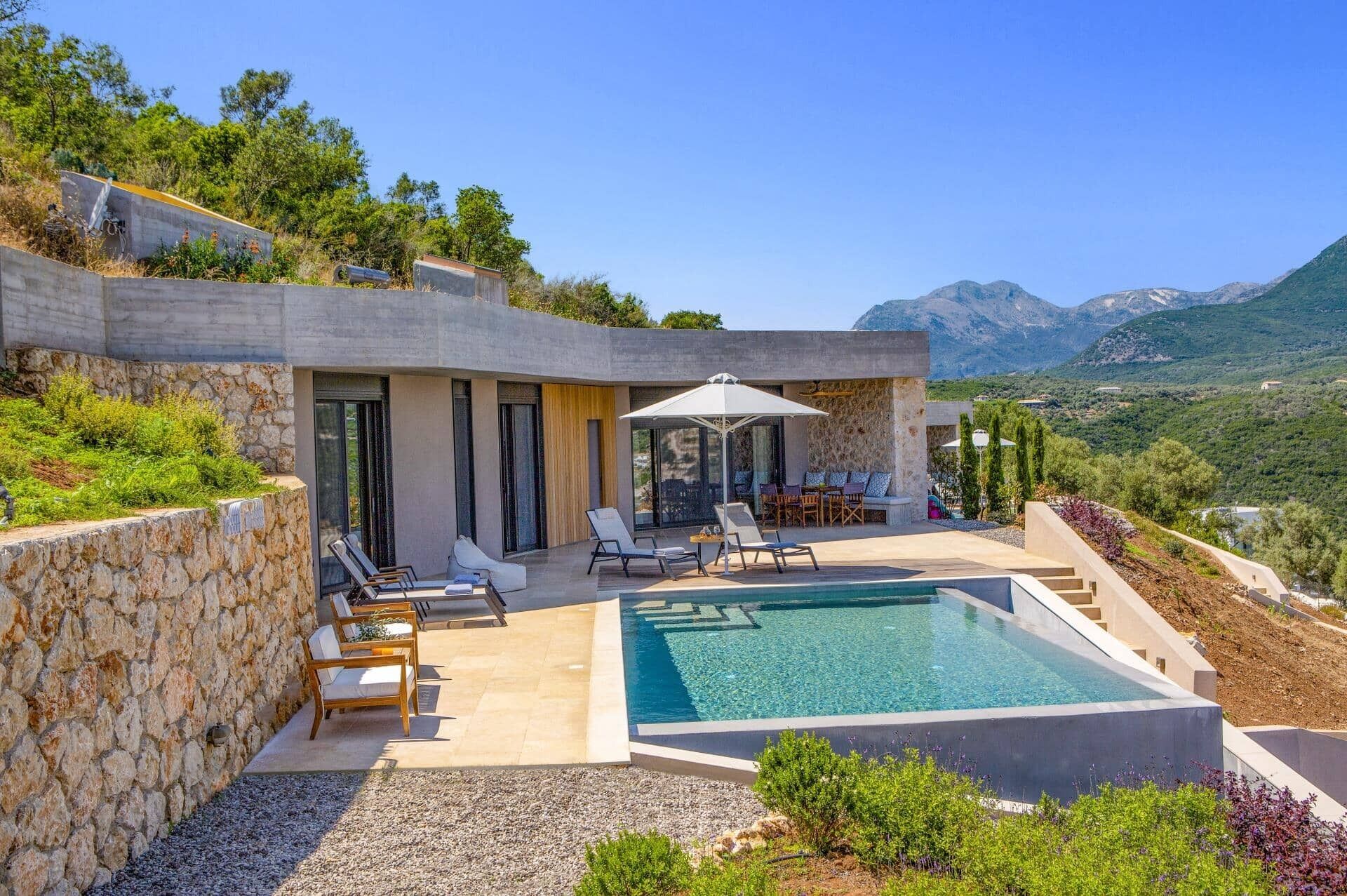 A modern villa with a swimming pool, outdoor seating, and a view of the mountains.