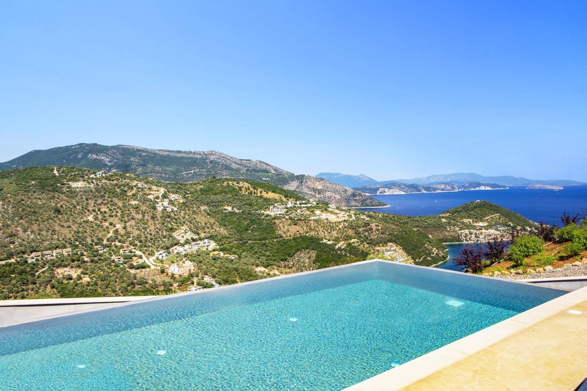 A swimming pool with a view of a coastal landscape, including hills and the sea.