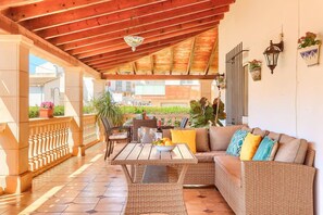 Une terrasse couverte, dotée de meubles en osier, d’un plafond en bois et de plantes en pot.