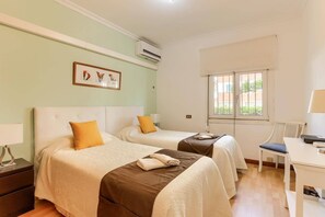 A hotel room with two beds, a desk, and a window with bars.