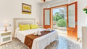 A bedroom with a bed, a nightstand, a lamp, a painting, and a view through a door.
