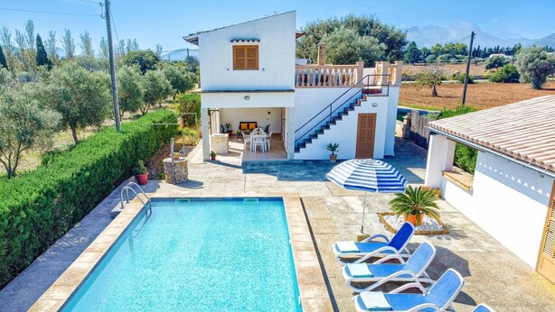 A poolside view of a two-story house with a swimming pool, lounge chairs, and a staircase leading to the upper floor.