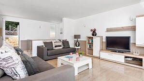 A modern living room with a grey sofa, white coffee table, and a flat-screen TV on a wooden stand. - Villa Grace by Villa Plus (Es Mercadal)