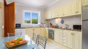 Een moderne keuken met een eethoek, met een glazen tafel, stoelen en een fruitmand.