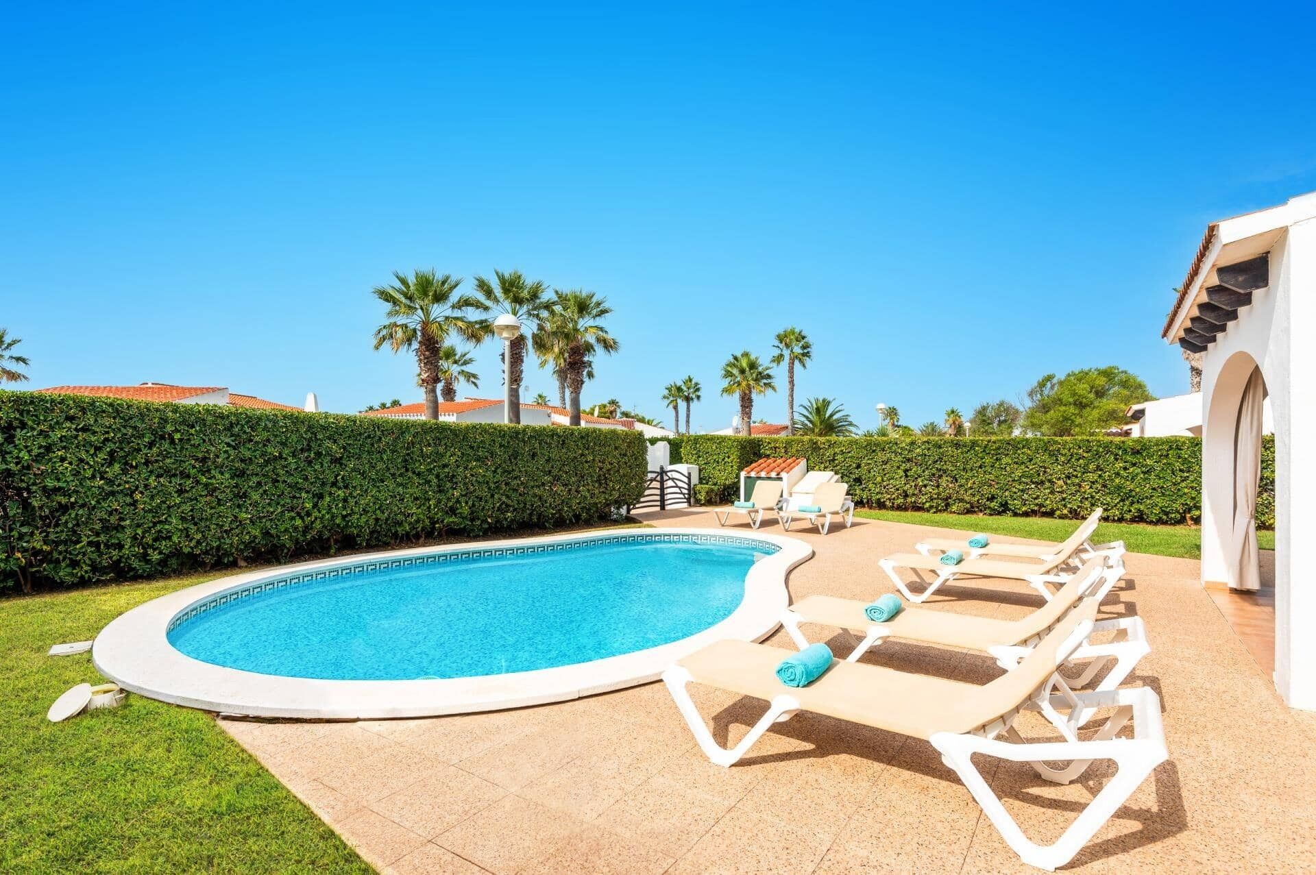 A swimming pool with lounge chairs and a hedge.