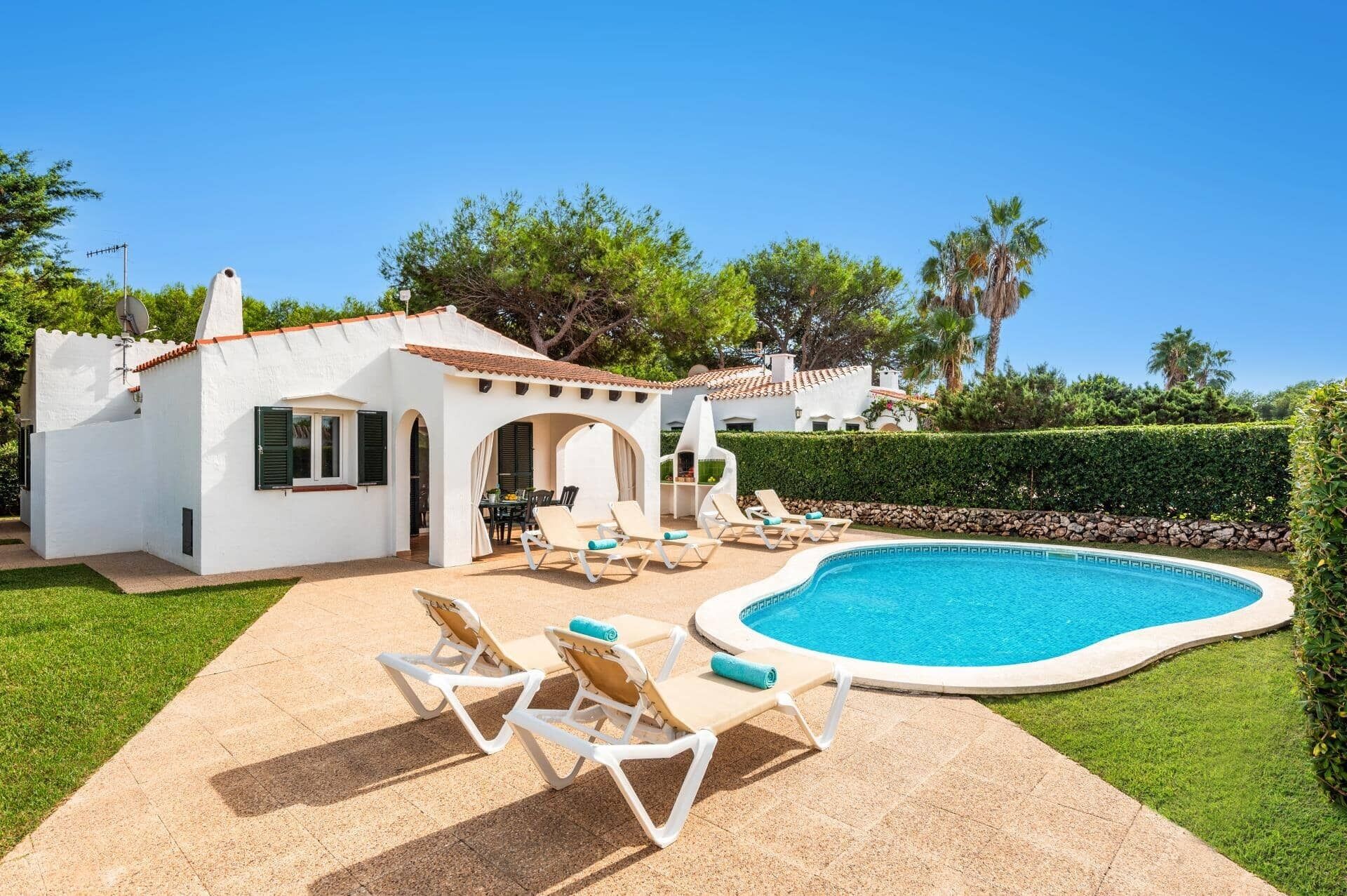 En hvid villa med swimmingpool, udendørs møbler og en velplejet have.