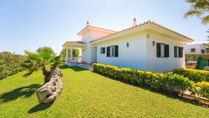 Une villa blanche avec un toit en tuiles, une véranda et une pelouse bien entretenue.