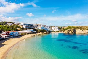 A coastal town with white buildings, a sandy beach, and clear blue waters.
