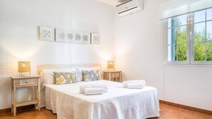 Une chambre à coucher avec un lit, deux tables de chevet, une fenêtre et des œuvres d’art murales.