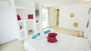 A hotel room with a bed, a small seating area, a shelf with decorative items, and a view of the outdoors. - Villa Gabriella by Villa Plus (Carovigno)