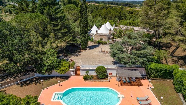 Vue aérienne d’une propriété dotée d’une piscine, de chaises longues et d’un bâtiment en pierre surmonté de toits coniques.