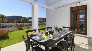 Un área de comedor al aire libre con una mesa dispuesta para cuatro personas, rodeada de sillas y vistas al paisaje.