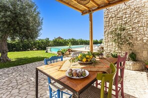 An outdoor dining area with a stone wall, a pool, and a view of the landscape. - Villa Ginevra by Villa Plus (Ispica)
