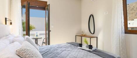 A bedroom with a bed, a bedside table with a lamp, a mirror, and a view of the outside.