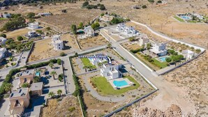 An aerial view of Villa Pandora Lindos, featuring modern architecture, a central swimming pool, and a surrounding landscape with sparse vegetation. - Villa Pandora Lindos by Villa Plus (Rhodes)