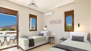 A hotel room with two beds, a balcony with a table and chairs, and a view of the cityscape. - Villa Pandora Lindos by Villa Plus (Rhodes)