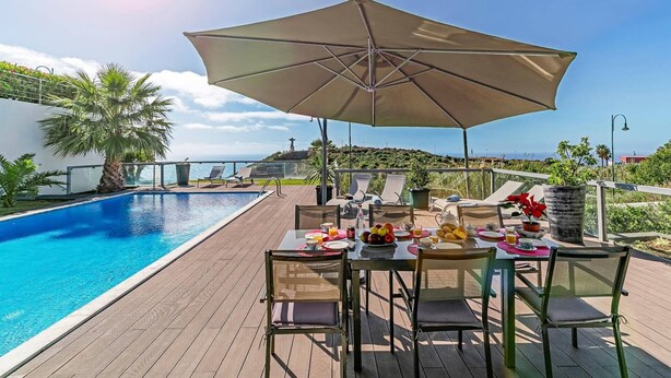 Ein Essbereich am Pool mit einem Tisch für zwei Personen, umgeben von Liegestühlen und einem großen Sonnenschirm.