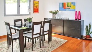 Ein Essbereich mit Holztisch und Stühlen, einem gemusterten Teppich, einer Kommode mit Dekoration und Bildern an der Wand.