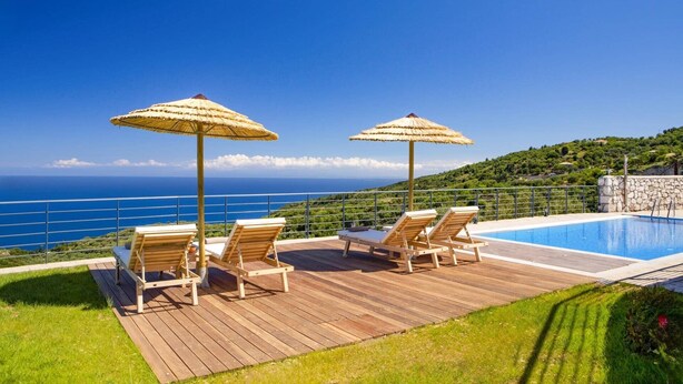 A wooden deck with lounge chairs and thatched umbrellas overlooking a pool and a scenic view of the ocean. - Villa Drimonas Erato by Villa Plus (Lefkada)