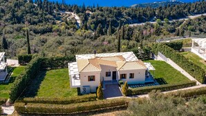 Eine weiße Villa mit Ziegeldach, umgeben von gepflegten Gärten und Blick aufs Meer.