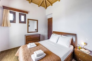 Quarto com cama de madeira, mesa de cabeceira com abajur, cômoda e espelho na parede.