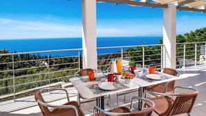 Eine Terrasse mit Tisch für zwei Personen, mit Blick auf das Meer und eine grüne Landschaft.