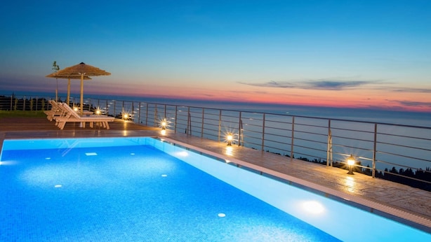 Ein Swimmingpool mit Liegestühlen und einem Strohdachschirm, mit Blick auf einen Sonnenuntergang über dem Meer.