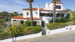 A white villa with a tiled roof, surrounded by lush greenery and a swimming pool. - Villa Curva do Monte by Villa Plus (Praia do Carvoeiro)